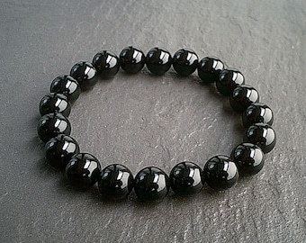 May include: A black onyx beaded bracelet with round beads. The bracelet is on a grey background.