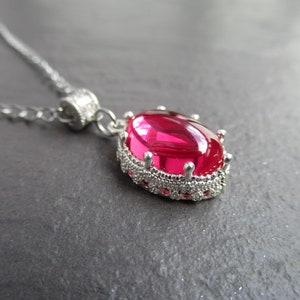 Op de afbeelding: Een zilveren ketting met een roze ovale edelsteen hanger in een zilveren kroonvormige setting.