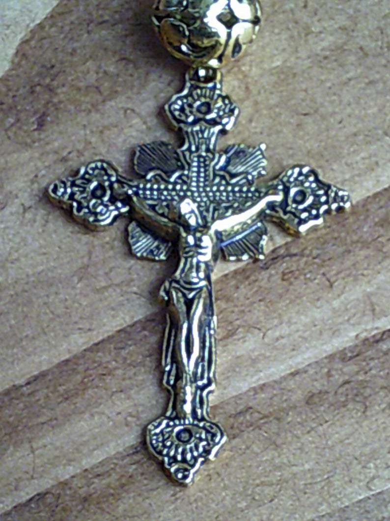 K&ouml;nnte beinhalten: Ein goldfarbenes Metallkreuz mit einem detaillierten Design. Das Kreuz zeigt eine Figur von Jesus Christus am Kreuz.