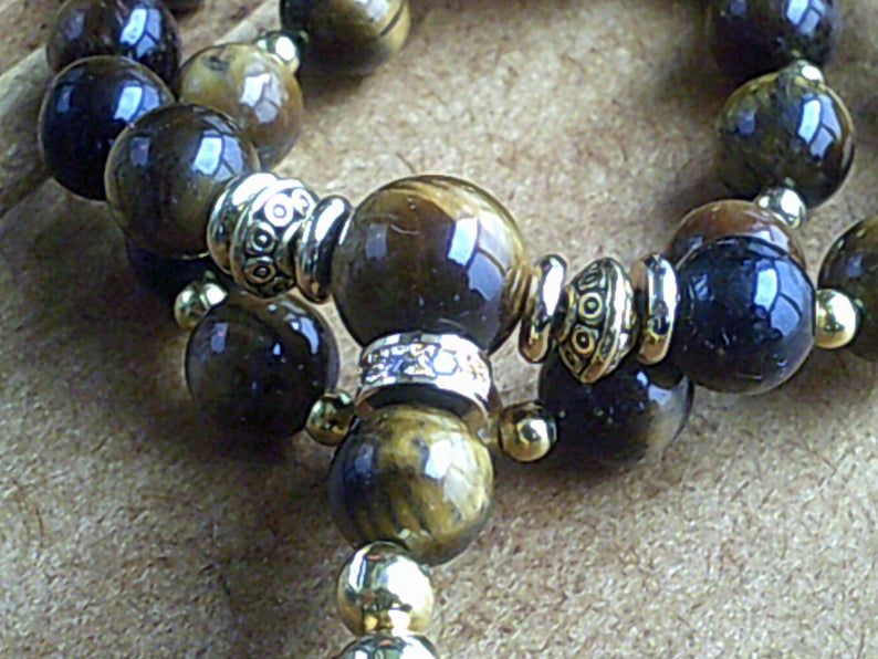 K&ouml;nnte beinhalten: Ein braunes und goldenes Perlenarmband mit silbernen Akzenten. Die Perlen sind aus Tigerauge und haben eine nat&uuml;rliche, polierte Oberfl&auml;che.