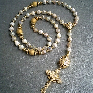 May include: A gold and grey gemstone rosary with a gold cross and a gold bead at the end.