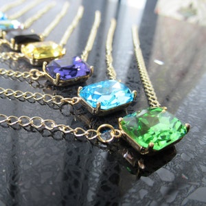 Może przedstawiać: Pięć złotych łańcuszków z różnokolorowymi, prostokątnymi kamieniami szlachetnymi. Kamienie są niebieskie, zielone, fioletowe, żółte i przezroczyste.