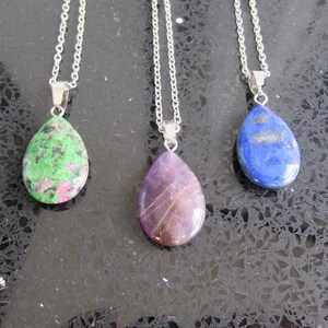 Puede incluir: Tres collares de cadena plateada con colgantes de piedra preciosa en forma de lágrima. Los colgantes son verdes, morados y azules.