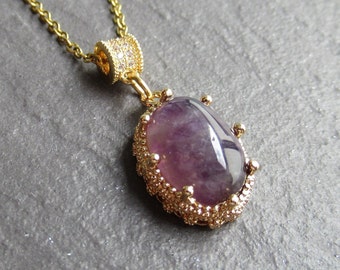 May include: A gold necklace with a purple gemstone pendant. The pendant is set in a gold filigree design.