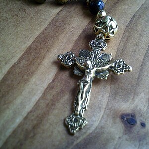 K&ouml;nnte beinhalten: Ein goldfarbenes Metallkreuz mit einer Jesus Christus-Figur darauf. Das Kreuz ist an einer Perlenkette befestigt.