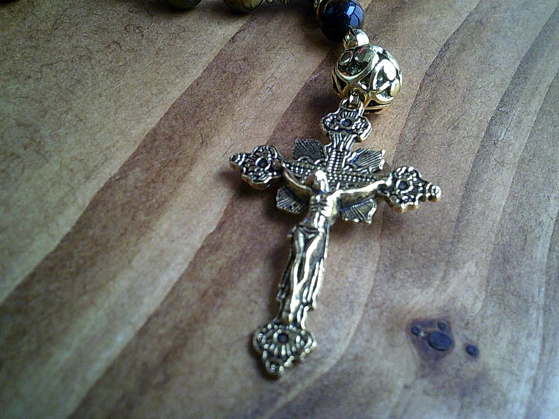 K&ouml;nnte beinhalten: Ein goldfarbenes Metallkreuz mit einer Jesus Christus-Figur darauf. Das Kreuz ist an einer Perlenkette befestigt.