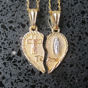 May include: Two gold heart-shaped pendants on chains, one with a crucifix and the other with a depiction of the Virgin Mary. The pendants are joined together to form a whole heart. The text "Te Amo" is inscribed on the pendants.