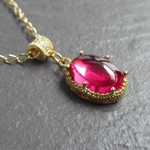 May include: A gold chain necklace with a pink oval-shaped gemstone pendant. The pendant is set in a gold filigree frame.