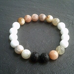 May include: A beaded bracelet featuring a mix of white, tan, and black beads. The bracelet includes white, light brown, and black lava stone beads. The bracelet is designed with a stretchable band.