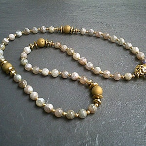 May include: A set of two necklaces made with light brown gemstone beads and gold accents. The longer necklace has a decorative gold pendant.