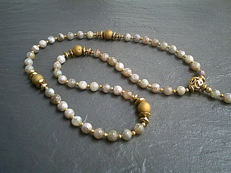 May include: A set of two necklaces made with light brown gemstone beads and gold accents. The longer necklace has a decorative gold pendant.