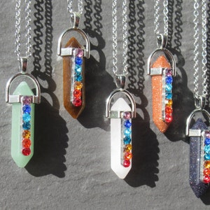 Może przedstawiać: Kolekcja sześciu naszyjników z wisiorkami z kamieni szlachetnych. Każdy wisiorek ma inny kolor, w tym zielony, brązowy, biały, pomarańczowy i ciemnoniebieski. Każdy wisiorek ma srebrną nasadkę i rząd kolorowych dżetów.