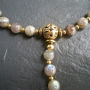 May include: A gold necklace with a decorative pendant and grey gemstone beads.