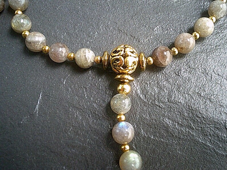 May include: A gold necklace with a decorative pendant and grey gemstone beads.