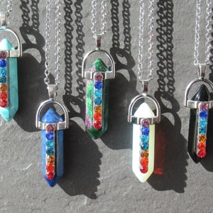 Może przedstawiać: Siedem srebrnych naszyjników z zawieszkami w kształcie kryształowych szpiców. Każdy wisiorek ma inny kolor kryształu z tęczą cyrkonii w środku.