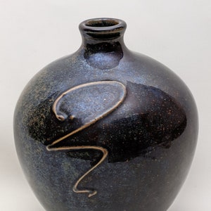 Puede incluir: Un jarrón de cerámica azul oscuro y marrón con un esmalte marrón claro y un diseño estilizado. El jarrón tiene un cuerpo redondo y un cuello estrecho.