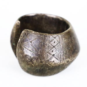 Könnte beinhalten: Ein silberfarbenes Armreif-Armband mit geätzten geometrischen Mustern. Das offene Manschettendesign weist eine Reihe von Diamant- und linearen Designs auf. Das Armband hat ein verwittertes Aussehen, was auf Alter oder eine Vintage-Ästhetik hindeutet.