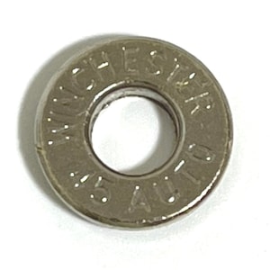 May include: A silver-colored metal disc with the words "WINCHESTER .45 AUTO" engraved on it. The disc has a hole in the center.