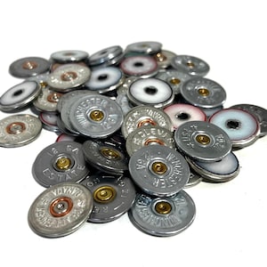 May include: A pile of silver shotgun shell casings with gold accents. Some of the casings have white or red accents. The casings are arranged in a random pattern.