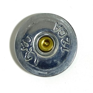 May include: A silver shotgun shell with a gold center and the number "12 GA" printed on the side.