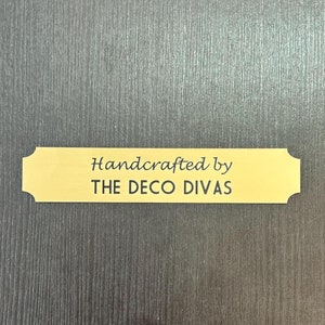 May include: A gold-colored metal plaque with the text "Handcrafted by THE DECO DIVAS" in black lettering.