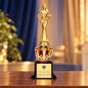 May include: A gold-colored trophy featuring a standing figure wearing a crown and holding a bouquet. The figure rests on a red and gold crown-shaped base atop a black pedestal. The plaque displays a crown icon and the text: Miss Queen 2024 Beautiful Inside and Out.