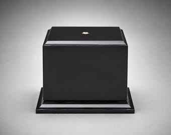 May include: A solid black rectangular display pedestal with a smooth, glossy finish. The base features a tiered, stepped design that extends slightly beyond the main body of the block, creating a stable foundation for showcasing various items.