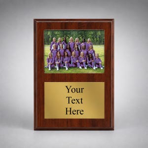 May include: A rectangular wooden plaque with a dark brown finish featuring a top inset photograph of a group of people wearing purple athletic uniforms standing in a grassy field and a bottom gold-colored metal plate with the text Your Text Here.