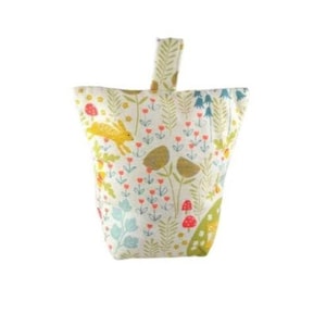 May include: A white doorstop with a floral pattern featuring yellow rabbits, red mushrooms, and green leaves. The doorstop has a loop handle.