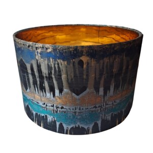 May include: A cylindrical lampshade with a black, blue and gold abstract pattern. The lampshade has a gold interior.