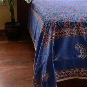 Könnte beinhalten: Eine blaue Bettdecke mit einem Blumenmuster in Rot und Rosa. Die Bettdecke hat einen dekorativen Rand mit einem sich wiederholenden Design. Der Stoff drapiert sich über die Seite des Bettes und zeigt die komplizierten Details.