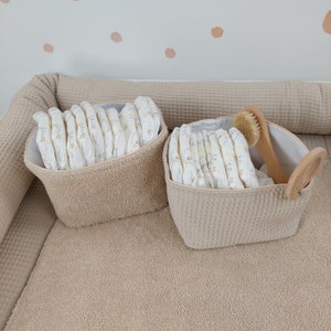 May include: Two beige fabric baskets with handles, one with a wooden handle, filled with nappies and a wooden brush.
