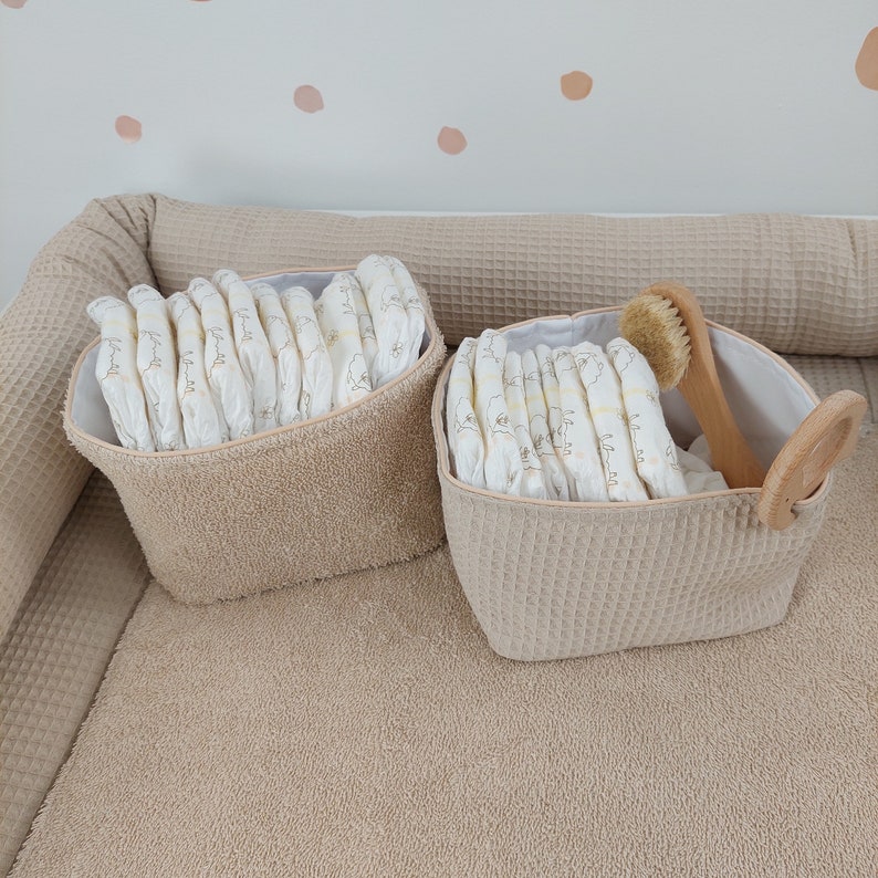 May include: Two beige fabric baskets with handles, one with a wooden handle, filled with nappies and a wooden brush.
