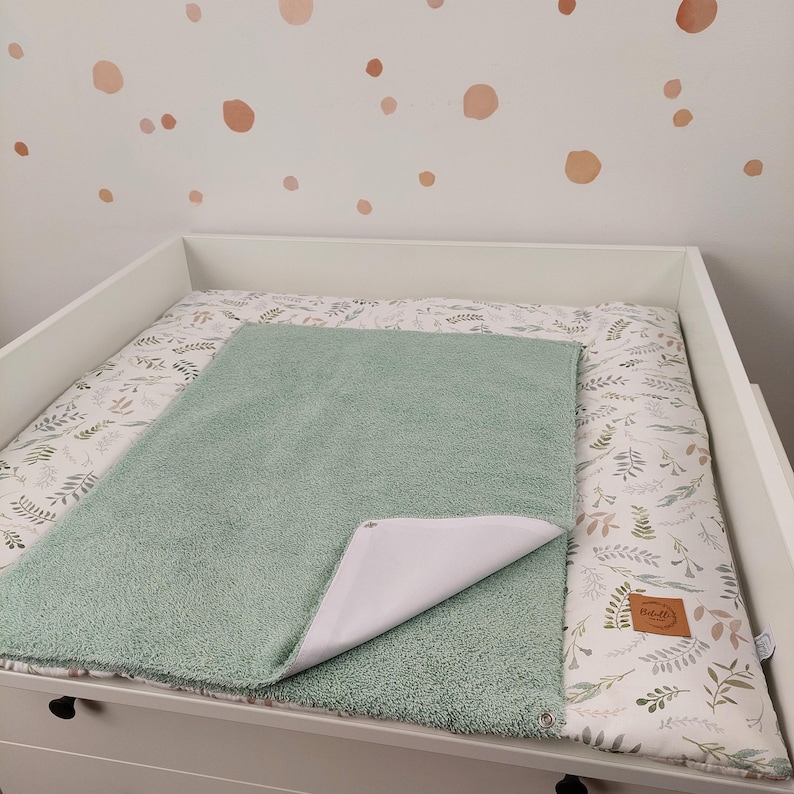 Puede incluir: Una funda para cambiador verde con un forro impermeable blanco. La funda est&aacute; hecha de tela suave y afelpada y est&aacute; dise&ntilde;ada para proteger el cambiador de derrames y manchas. La funda se muestra en un cambiador con un cambiador de estampado floral debajo.