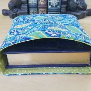 May include: A blue and green paisley patterned book cover with a green and white polka dot lining. The cover is folded over a book.