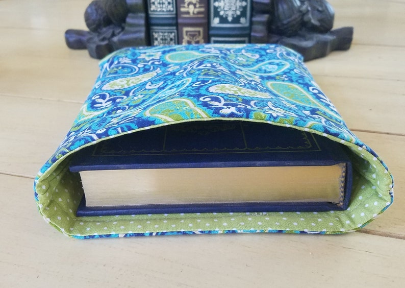 May include: A blue and green paisley patterned book cover with a green and white polka dot lining. The cover is folded over a book.