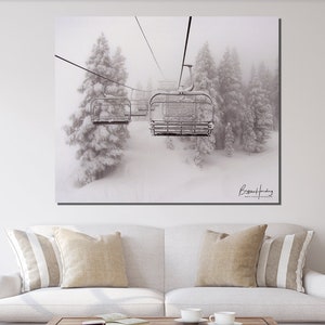 May include: Black and white photograph of a ski lift ascending through a snowy forest. The image features a row of ski lift chairs, with snow-covered evergreen trees in the background. The artist's signature is visible in the lower right corner.