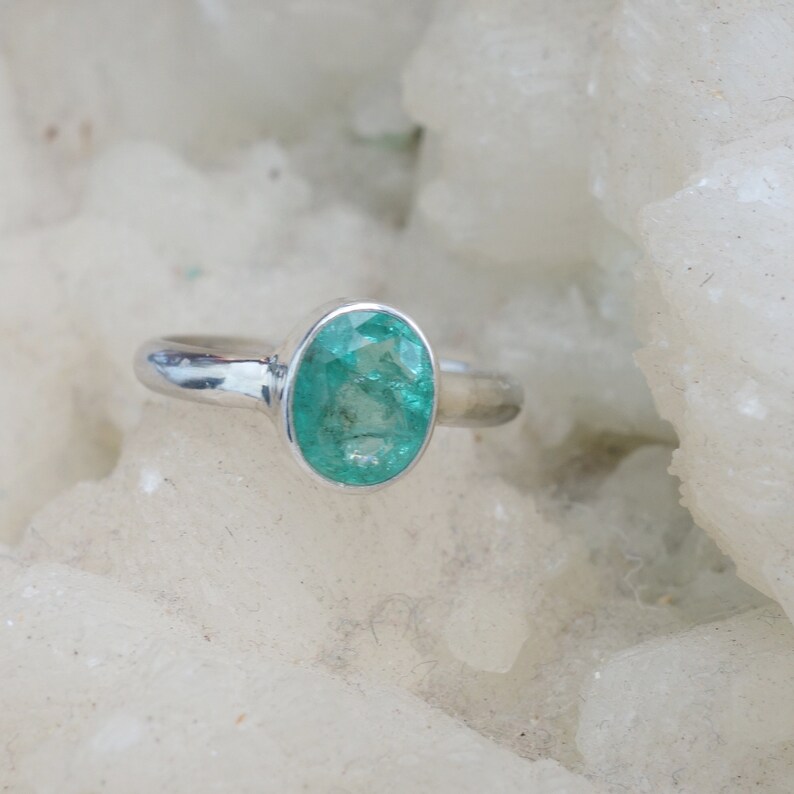 May include: A silver ring with a green oval emerald gemstone.