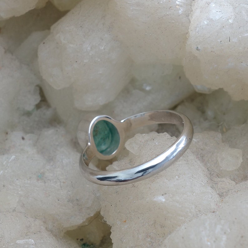 May include: A silver ring with a green oval gemstone set in the center. The ring is on a white background.