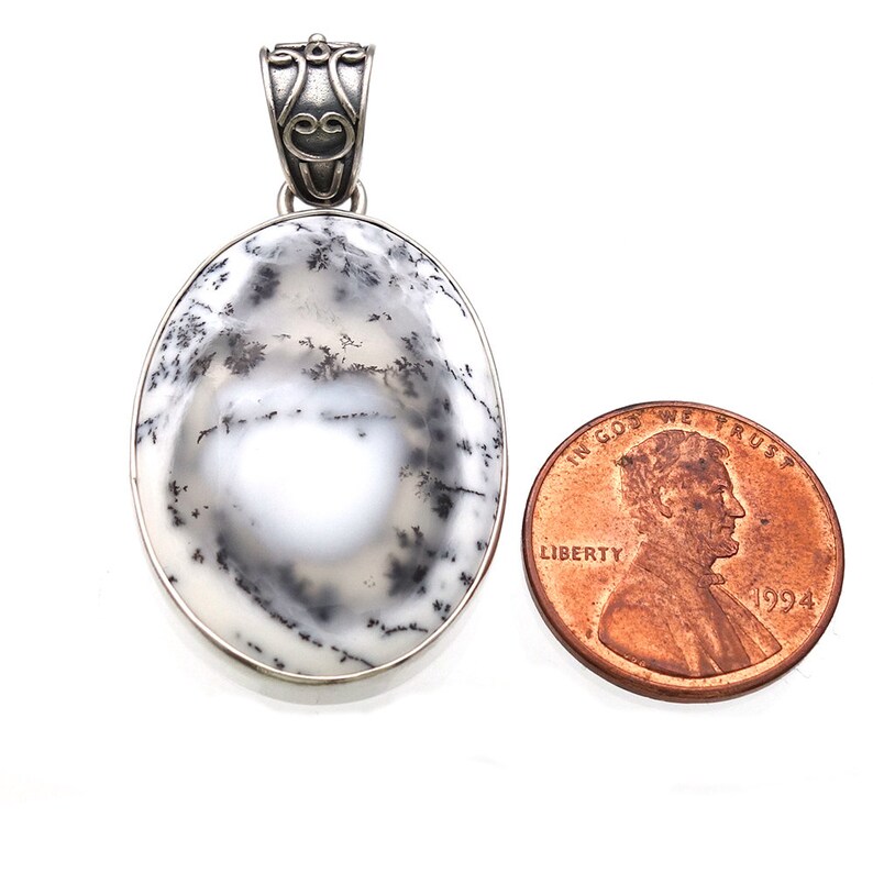 May include: A silver pendant featuring a white and gray dendritic agate oval stone with a silver bail. The pendant is approximately the size of a US penny.