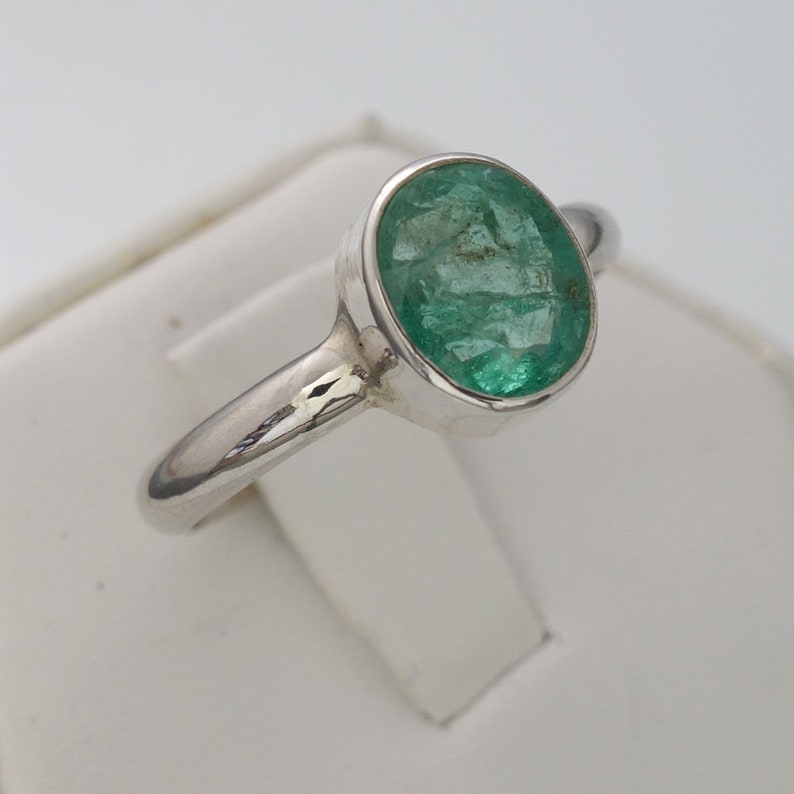 May include: A silver ring with a green oval emerald gemstone.