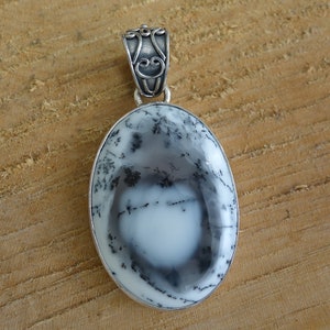 May include: A silver pendant featuring a white and black dendritic agate stone with a detailed silver bail.