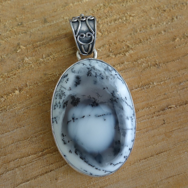 May include: A silver pendant featuring a white and black dendritic agate stone with a detailed silver bail.
