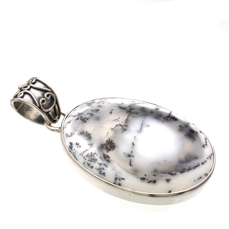 May include: A silver pendant with a white and black dendritic opal stone. The pendant has a detailed silver bail.