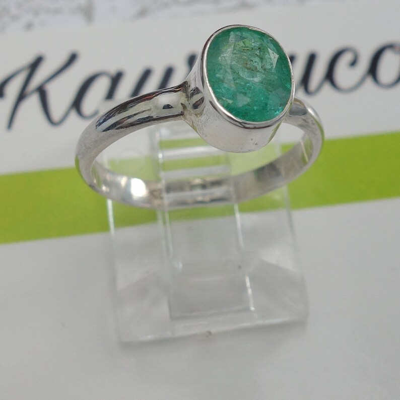 May include: A silver ring with a green oval emerald gemstone.
