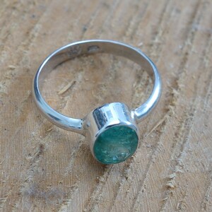 May include: A silver ring with a green gemstone. The ring is set with a round, faceted emerald.