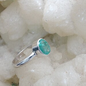May include: A silver ring with a green oval emerald gemstone.