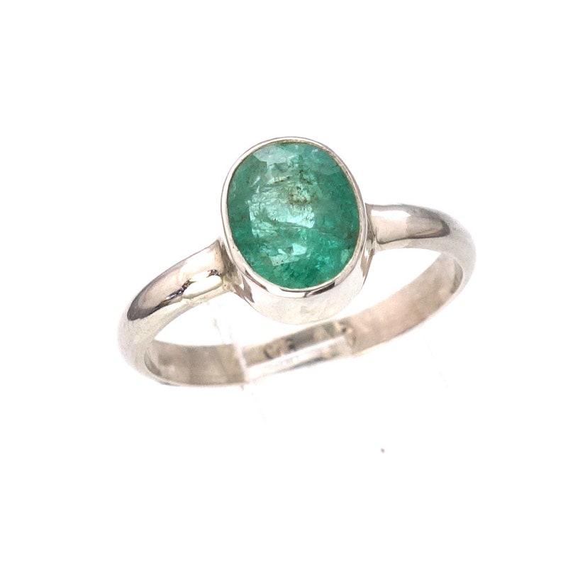 May include: A silver ring with a green oval emerald gemstone.