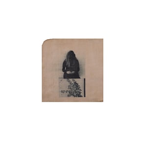 May include: A square piece of light brown fabric featuring a black and white printed image. The top portion displays a person with long hair sitting down, while the bottom portion shows a detailed botanical illustration of a leafy plant branch.