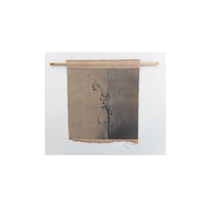 Puede incluir: Un tapiz de pared textil con una ilustración botánica. La obra de arte está impresa en una tela de color beige con un borde sin rematar en la parte inferior. Se utiliza una clavija de madera para colgarla. La ilustración representa una planta con tallos y flores delicados.